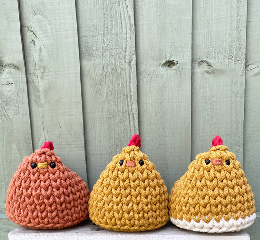 Three Henrietta the hen chicken doorstops in different colour's against a wooden background